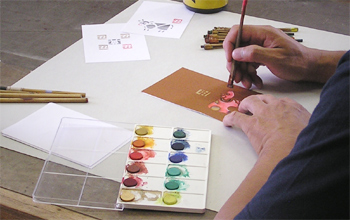 型紙で手作り年賀状を作成（絵の具と刷毛で彩色）している場面